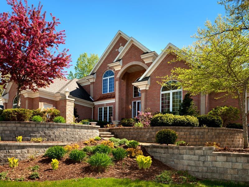 Large brick house with arched windows, manicured landscaping, and trees in front yard