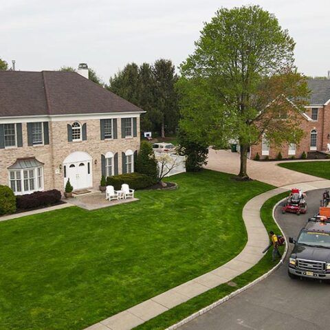 Suburban townhouse with a large green lawn, curved sidewalk, and parked cars on a quiet street.