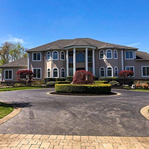 Large beige apartment building with arched windows and circular driveway under a clear blue sky