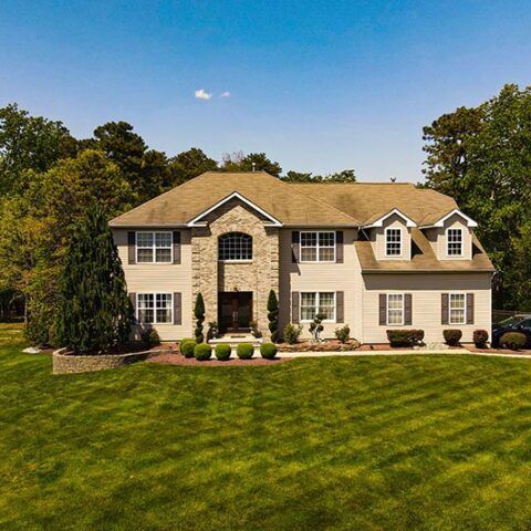 Large beige suburban house with white trim and a manicured green lawn under a clear blue sky