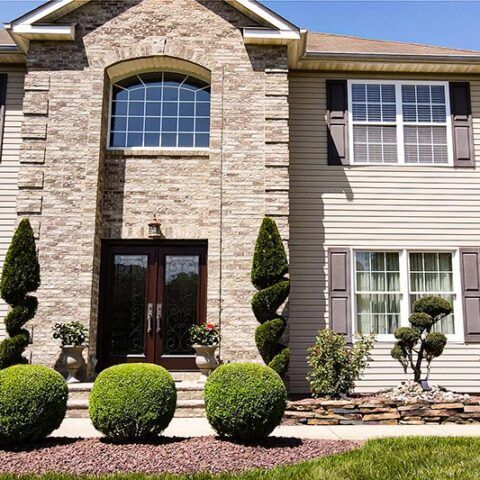Suburban house facade with stone entry, arched window, double doors, and trimmed shrubs in front yard