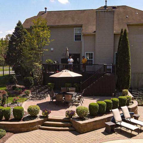 Landscaped backyard patio with umbrella, lounge chairs, and a raised deck beside a house