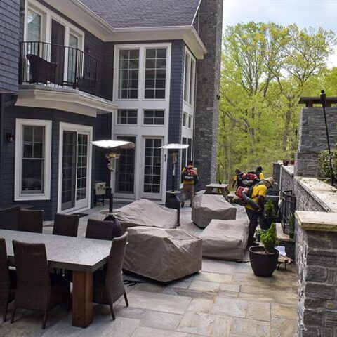 Patio with outdoor furniture beside a house, with firefighters carrying equipment near the walkway