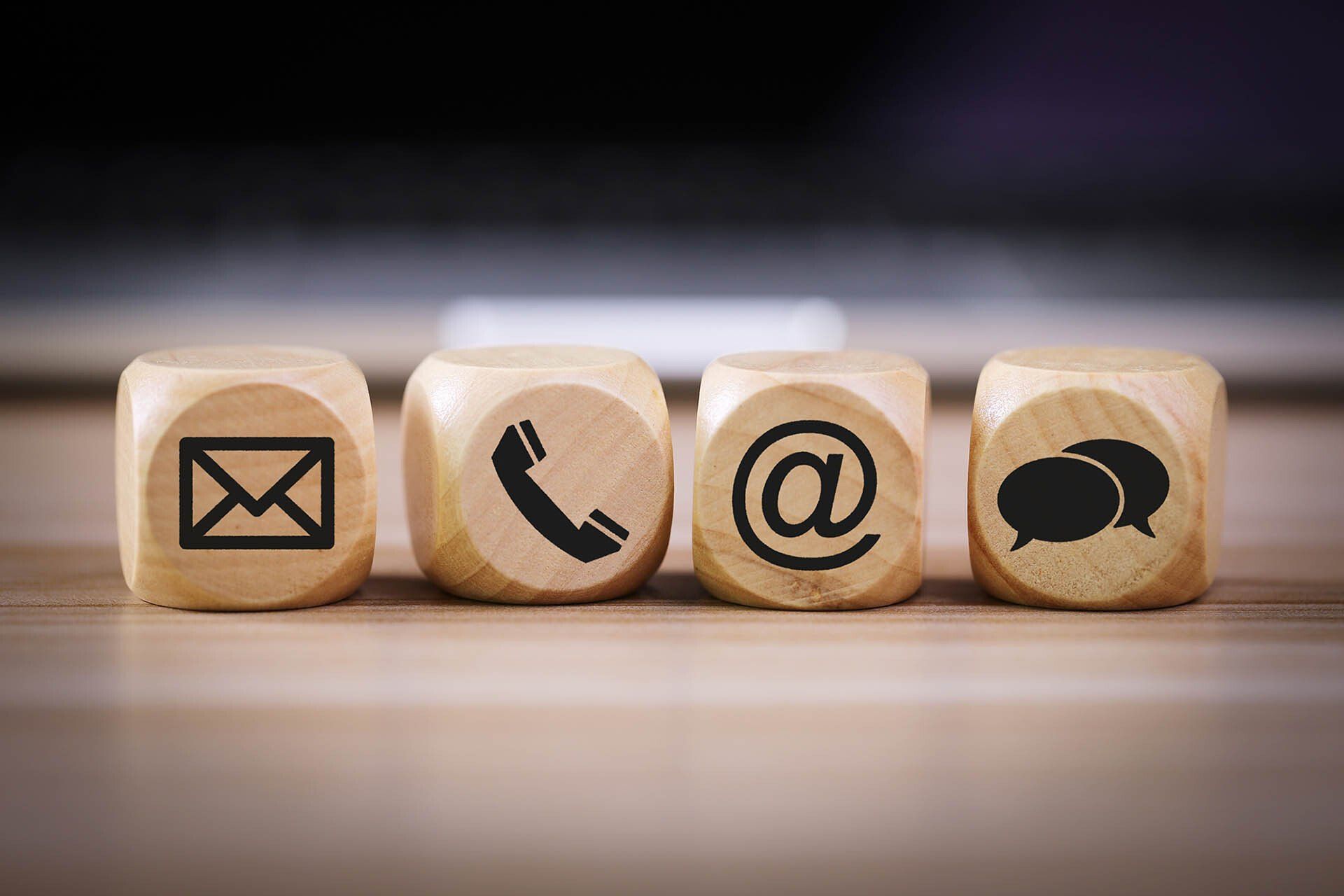 Quattro blocchi di legno con icone di contatto: busta, telefono, e-mail e fumetti.