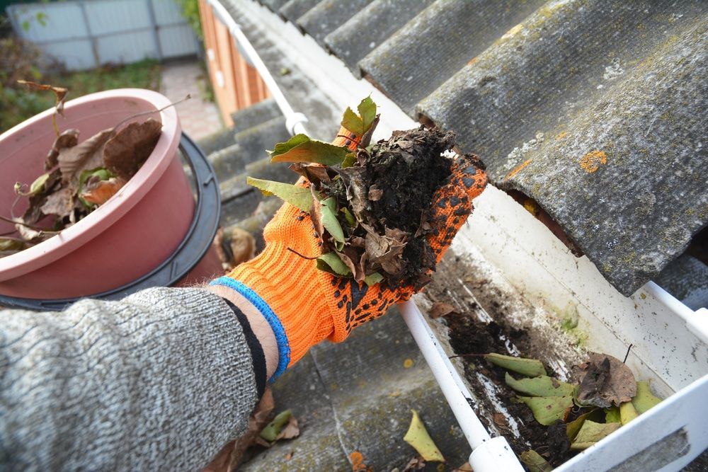 A person wearing orange gloves is cleaning a gutter on a roof.