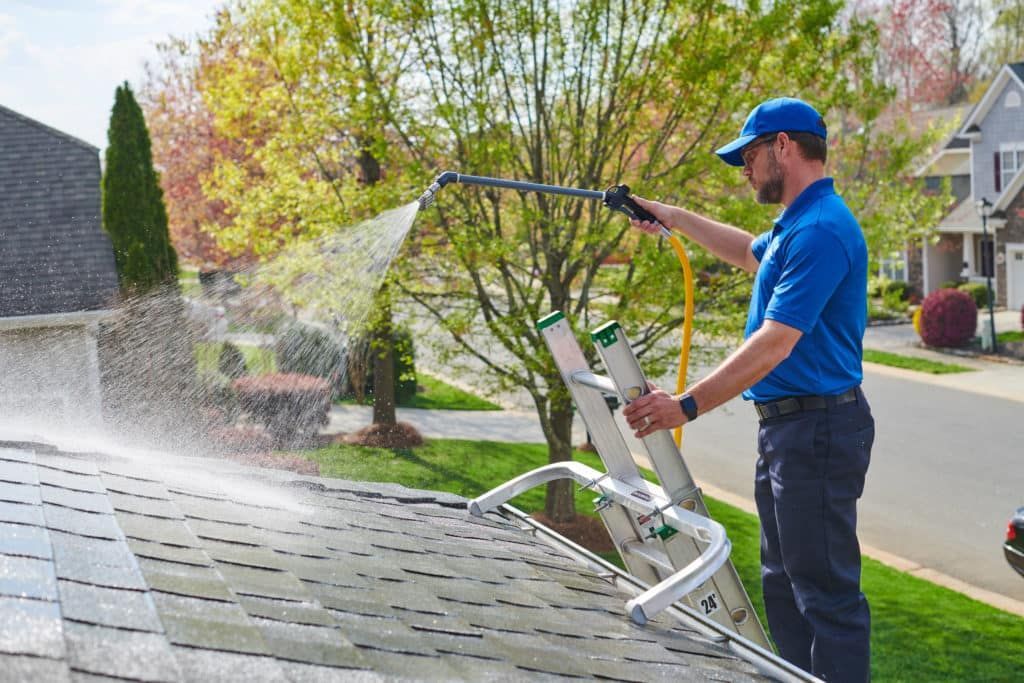 A man is cleaning the roof of a house with a high pressure washer.