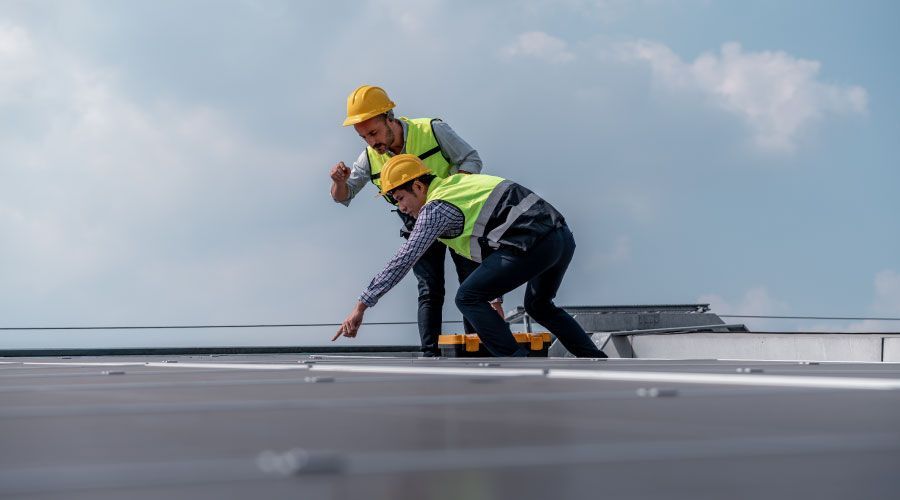 Two construction workers are working on the roof of a building.