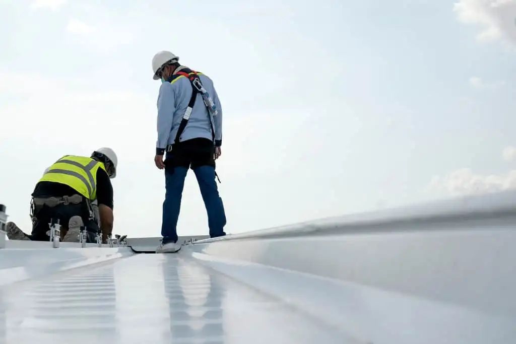 Two construction workers are working on the roof of a building.