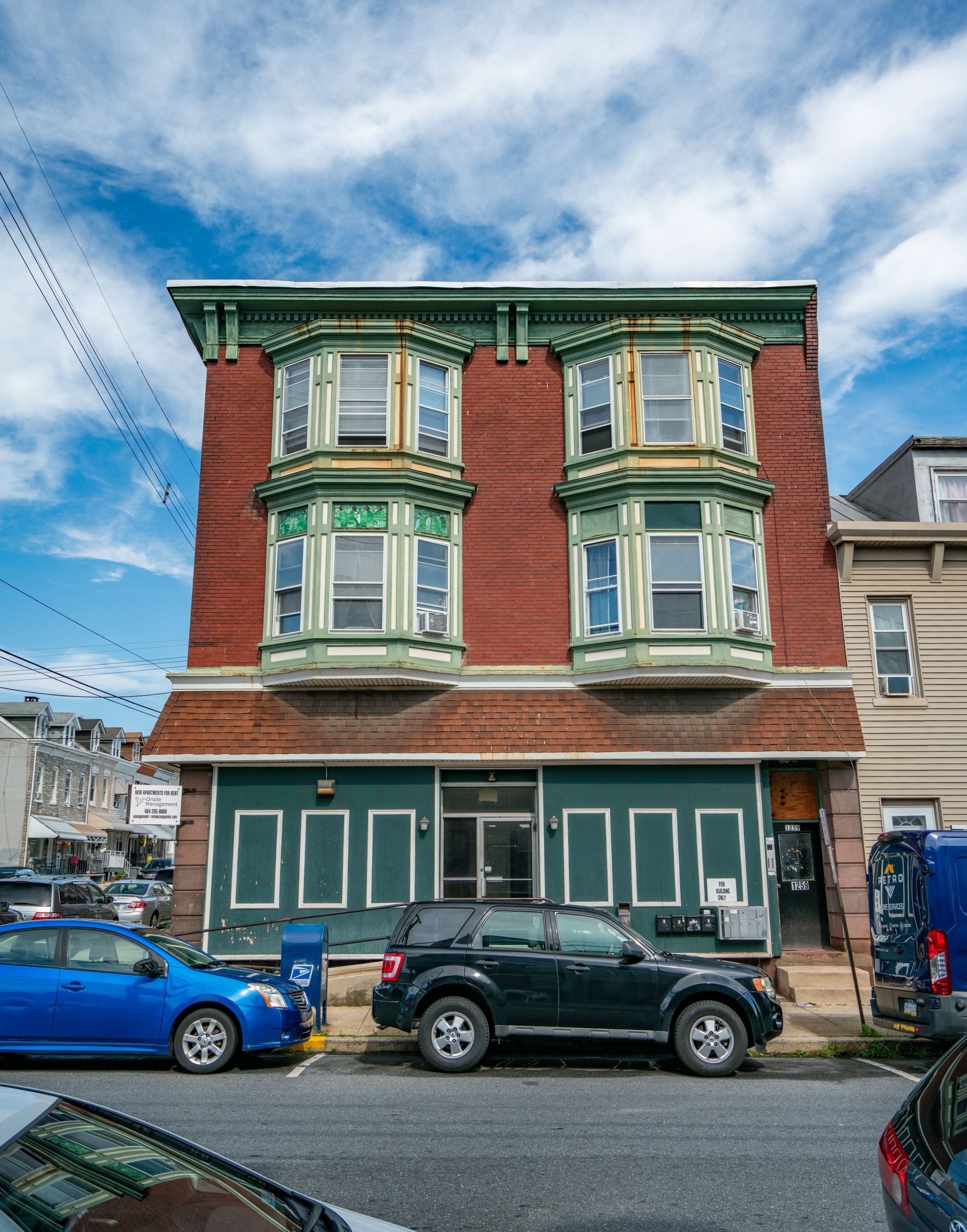 Photo of a 3 story building, red brick and green elements, with windows that extend beyond the building 