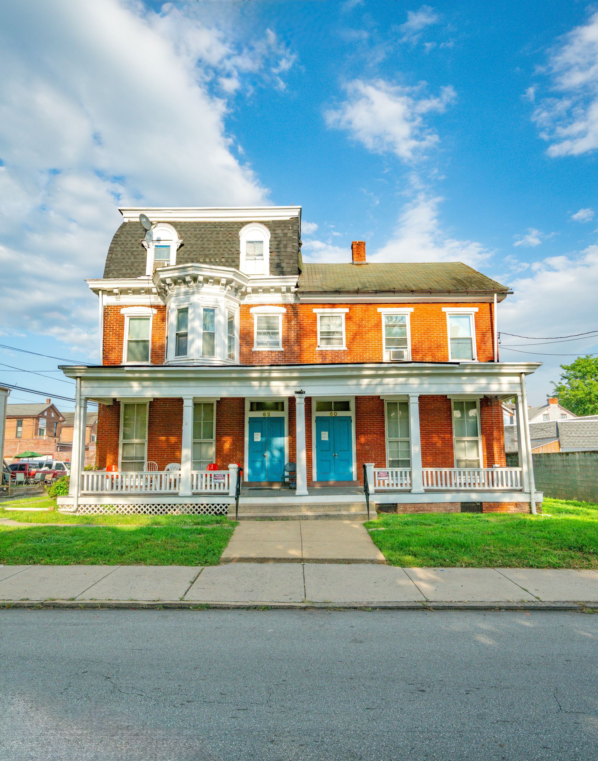 Photo of an 19th century or early 20th century home, 3 stories featuring red brick, combined with white and black elements, seen from the street