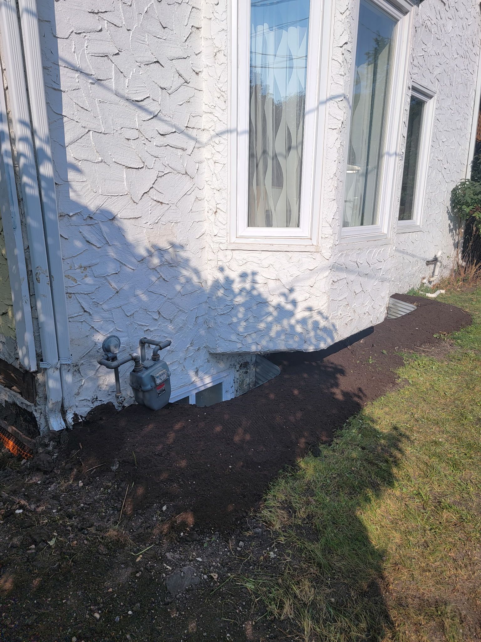 A white stucco house exterior featuring a bay window, a gas meter, and a fresh layer of mulch along the foundation.