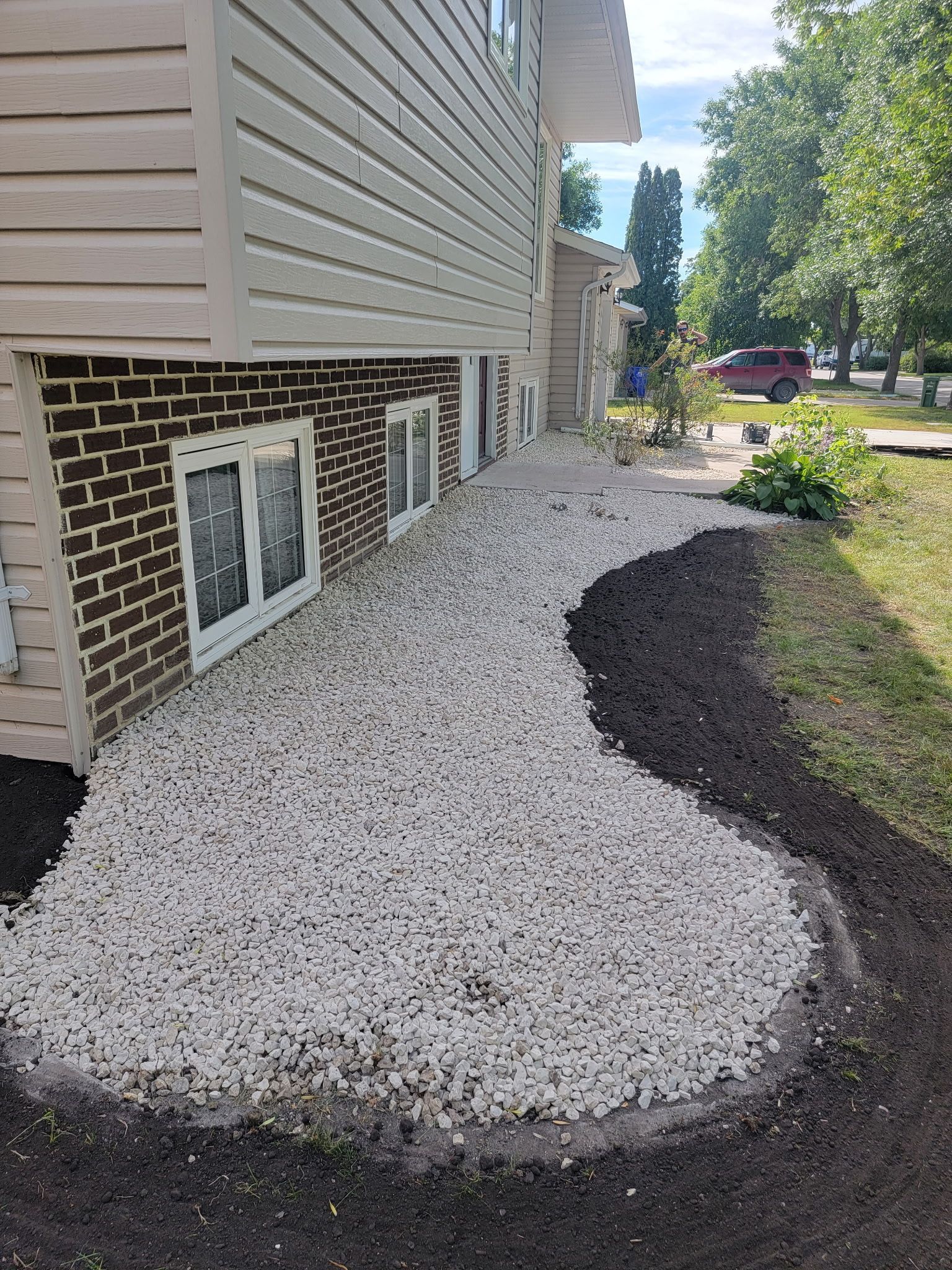 White gravel covers a landscape bed along the brick-covered basement wall of a house, edged with dark mulch.