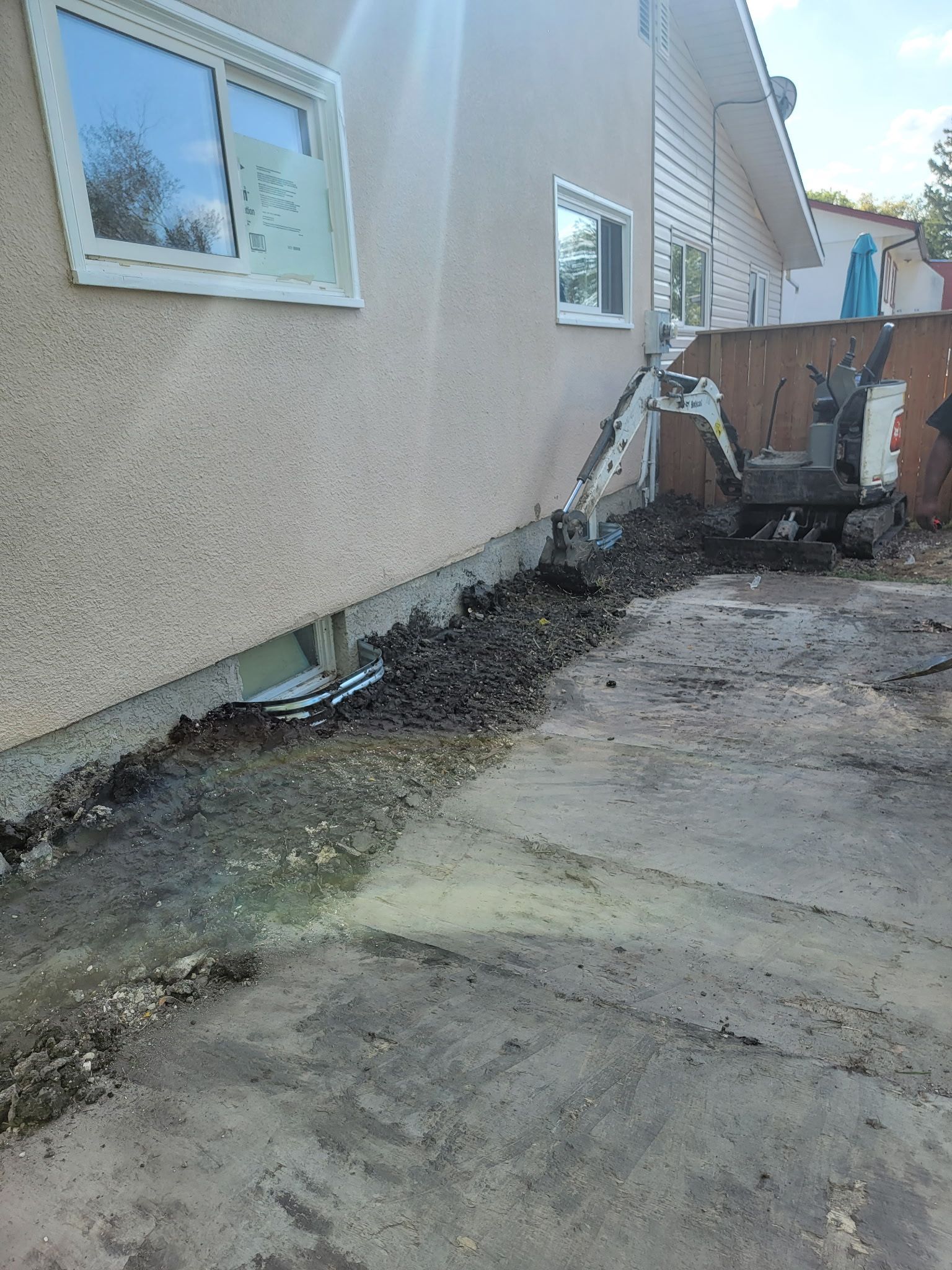 A compact excavator parked next to a house foundation undergoing exterior excavation work.
