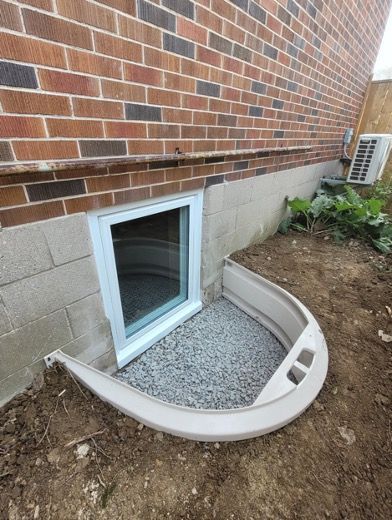 Installed egress window with window well and gravel drainage beside a Winnipeg home