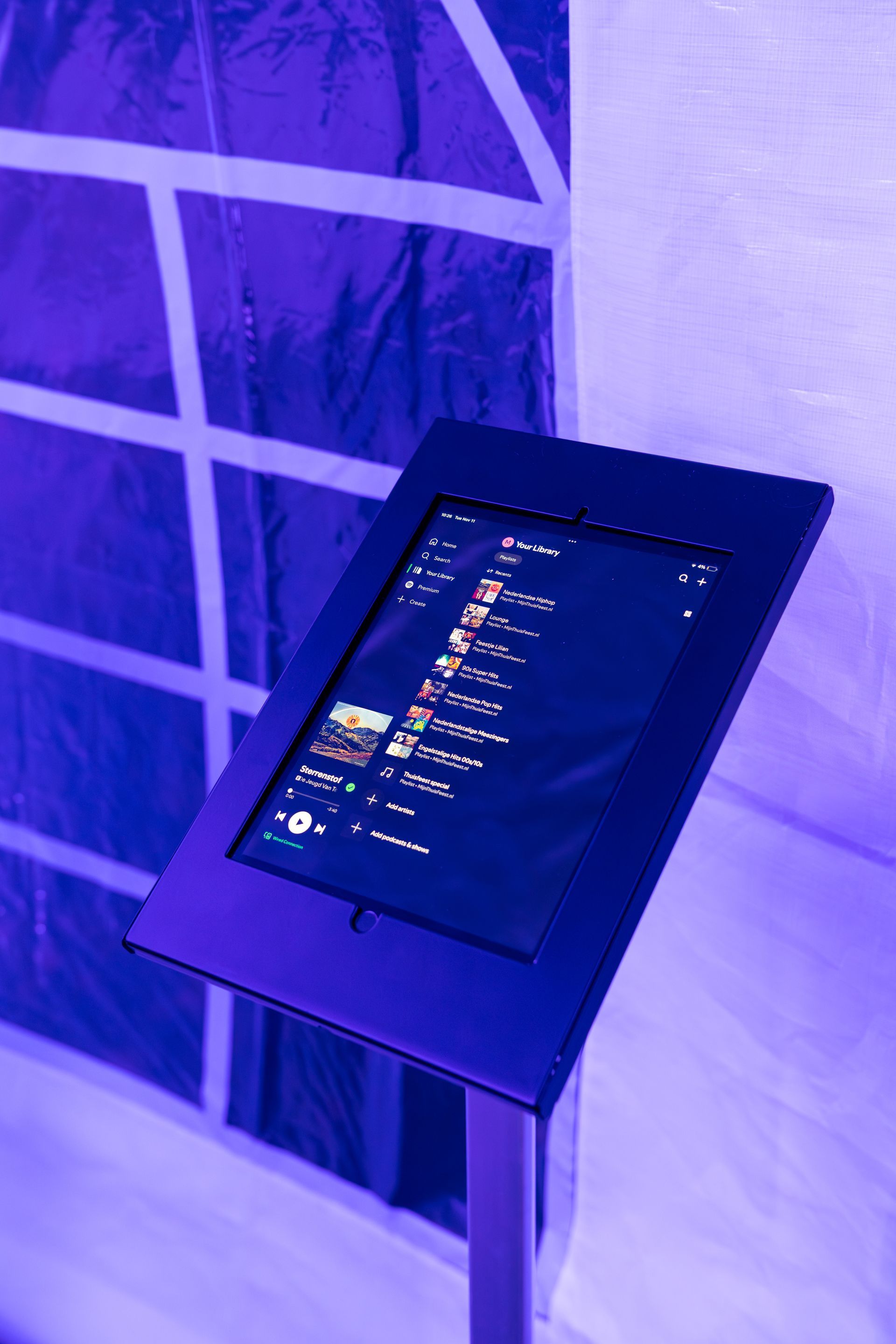 Een hand bedient een digitaal touchscreen dat op een standaard staat tijdens een buitenevenement dat in blauw licht is verlicht.