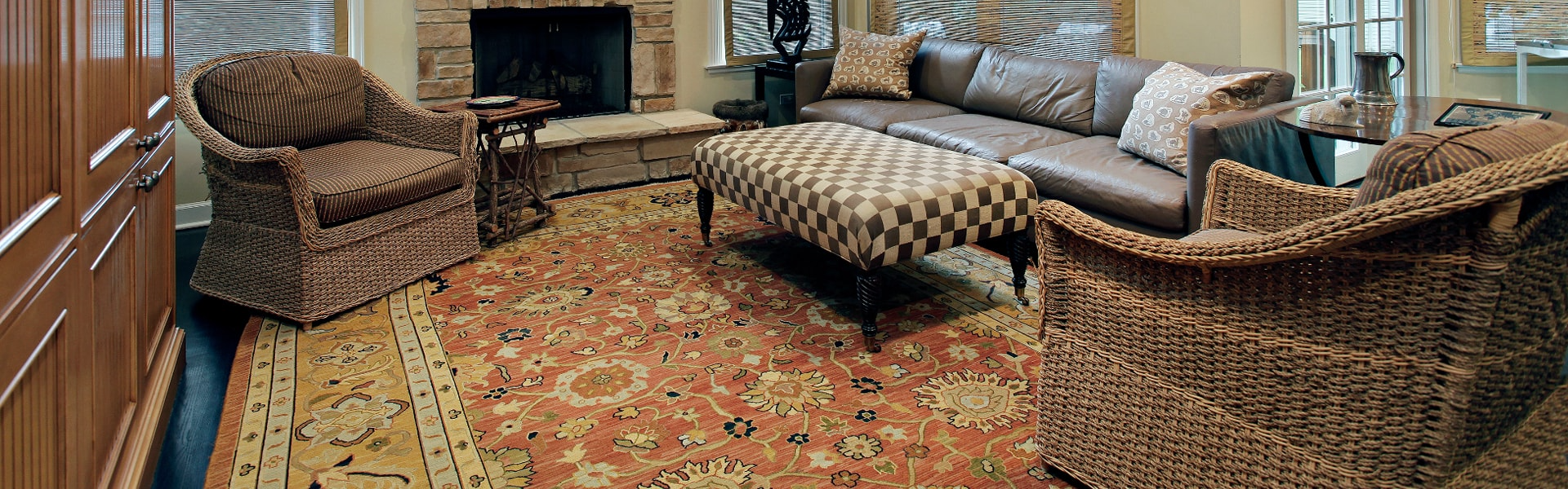 Cozy living room with wicker chairs, patterned rug, fireplace, and blue sofa around a glass coffee table