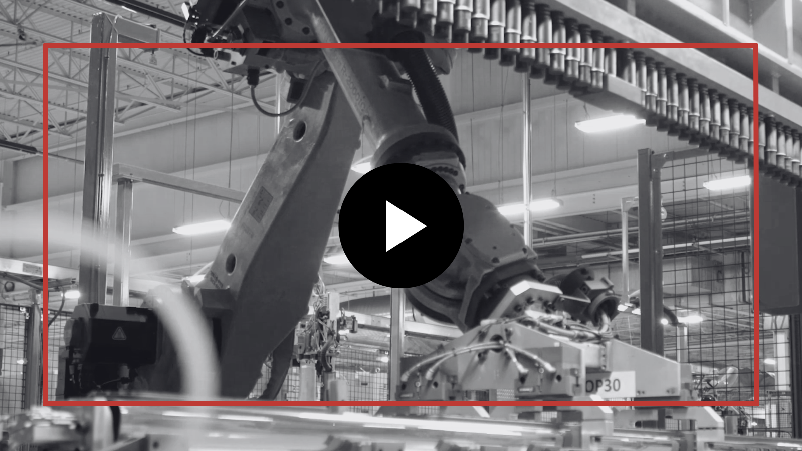 Factory robot arm assembling machinery in an industrial workshop, shown in grayscale with a play button overlay