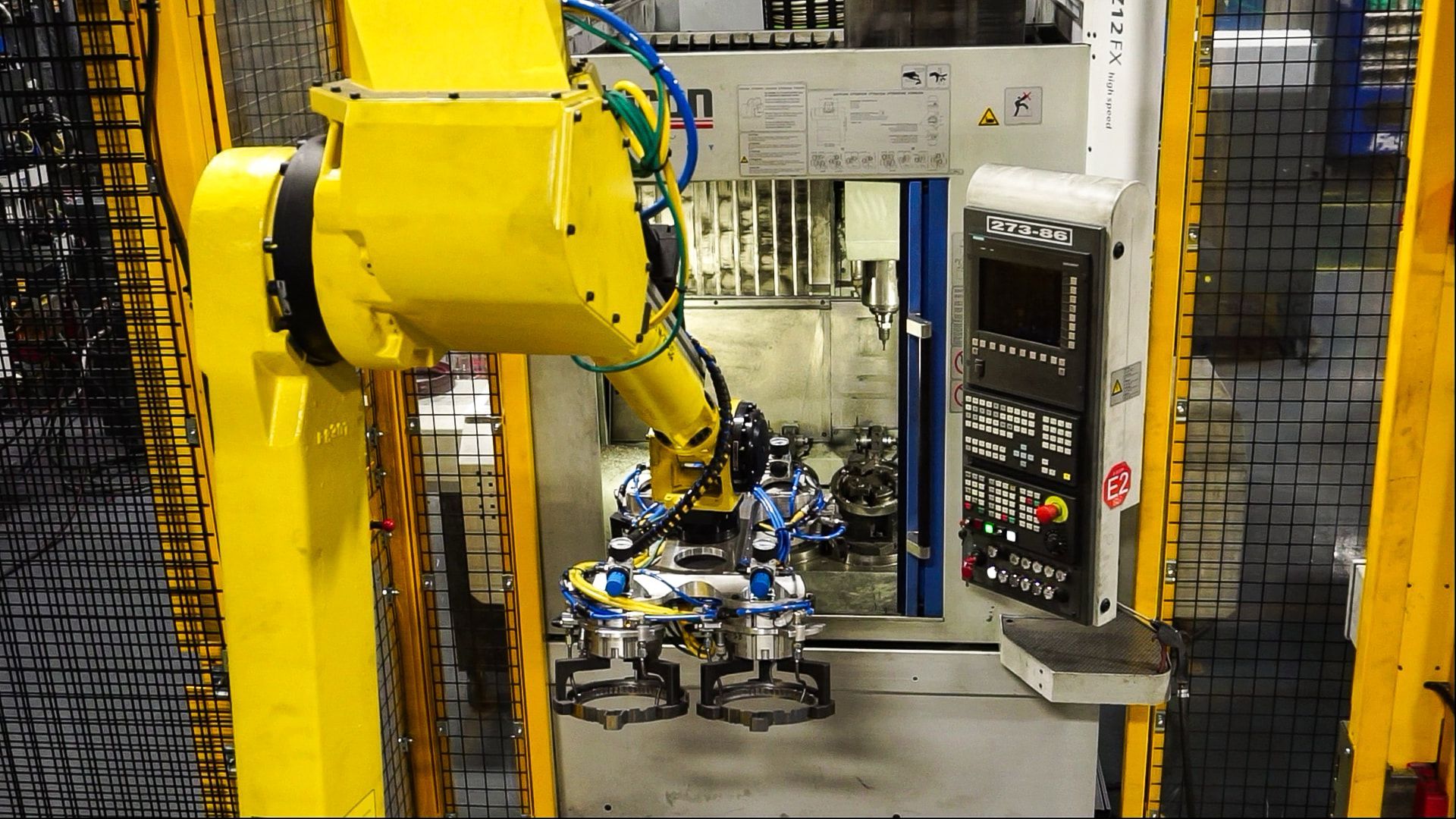 Yellow industrial robot arm assembling parts on a factory line inside a fenced work cell.