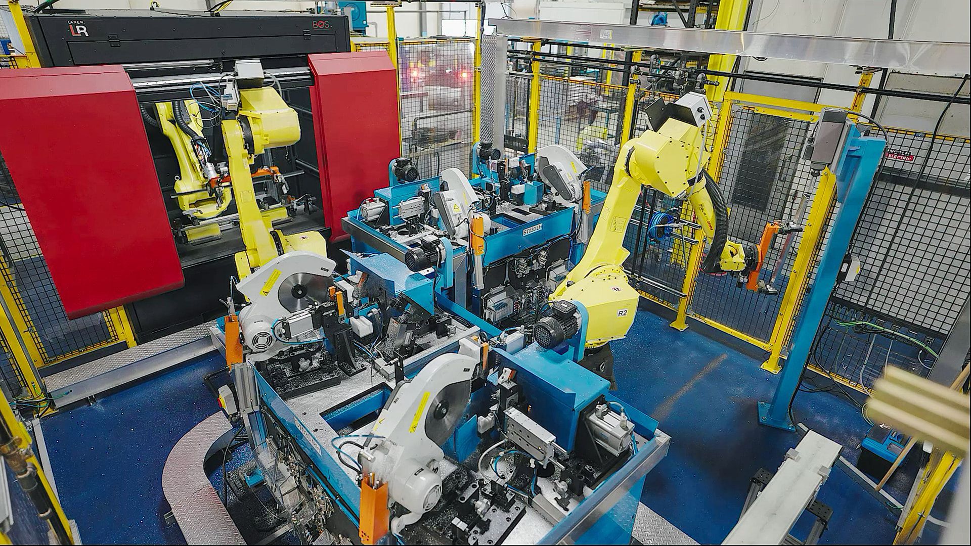 Robotic arms assembling parts on a factory production line with yellow safety fencing.