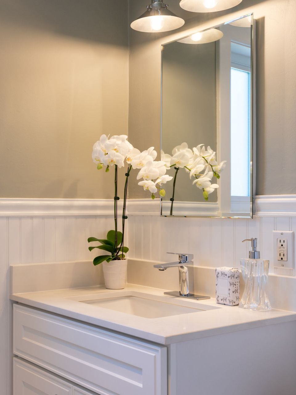 A bathroom with a sink , mirror and flowers on the counter.