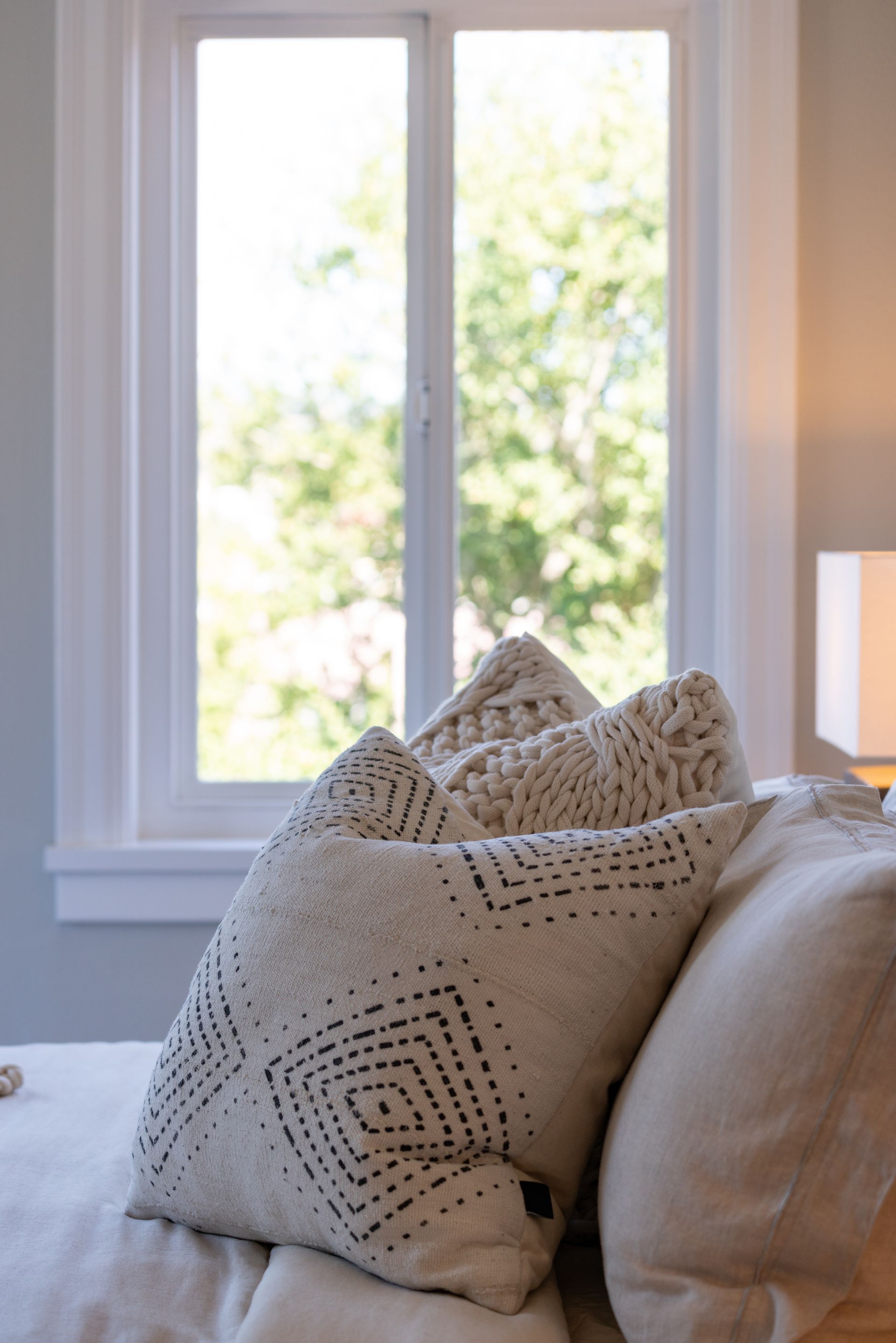 A bed with pillows and a lamp in front of a window.