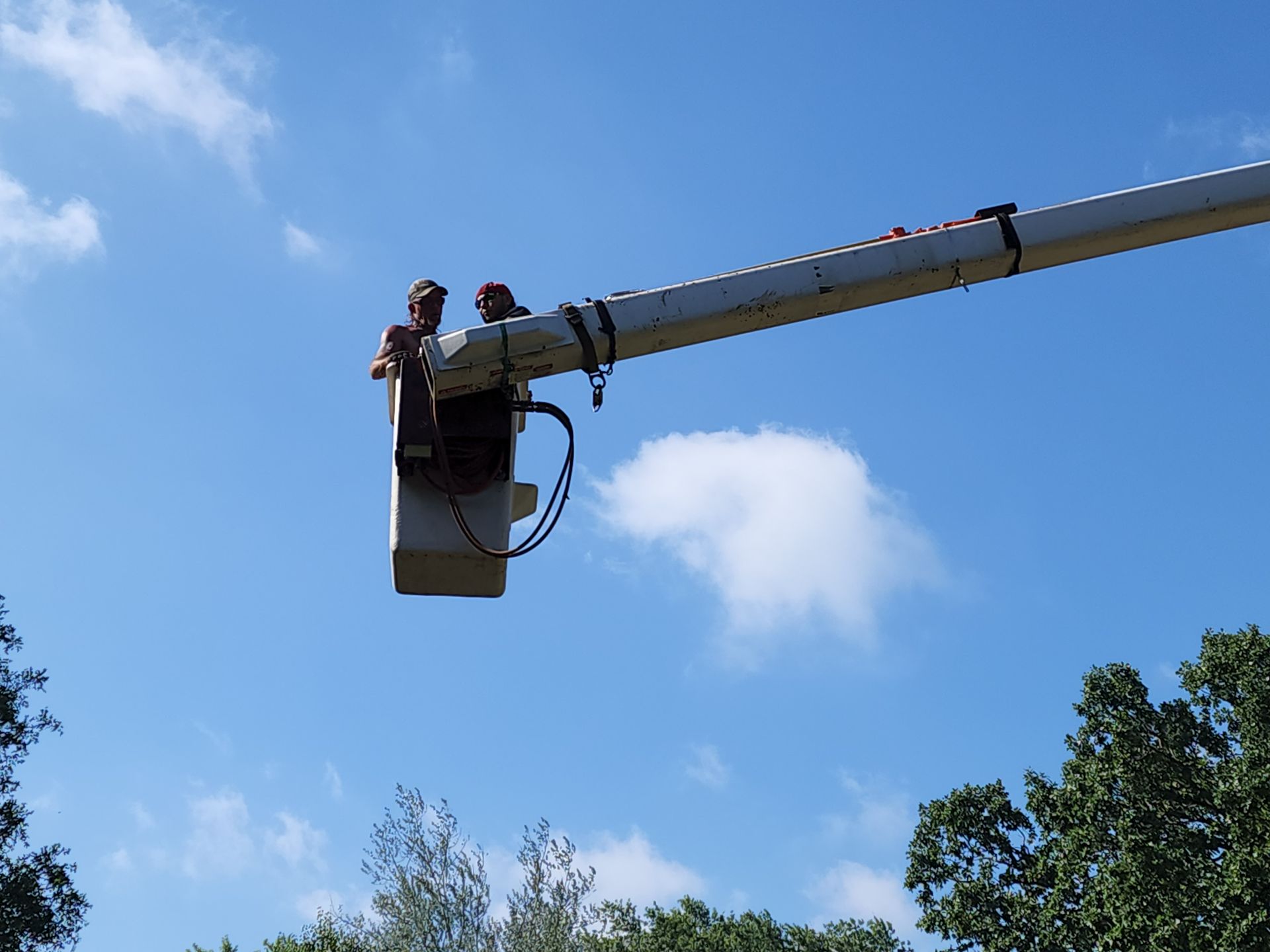 A man is sitting in a bucket on a crane.