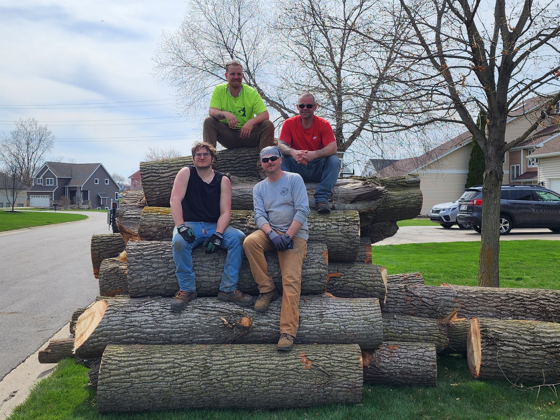 A group of men are sitting on top of a pile of logs.