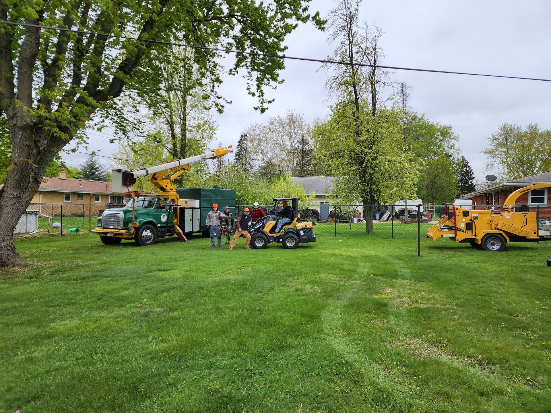 A group of people standing next to a truck and a tractor in a grassy field.
