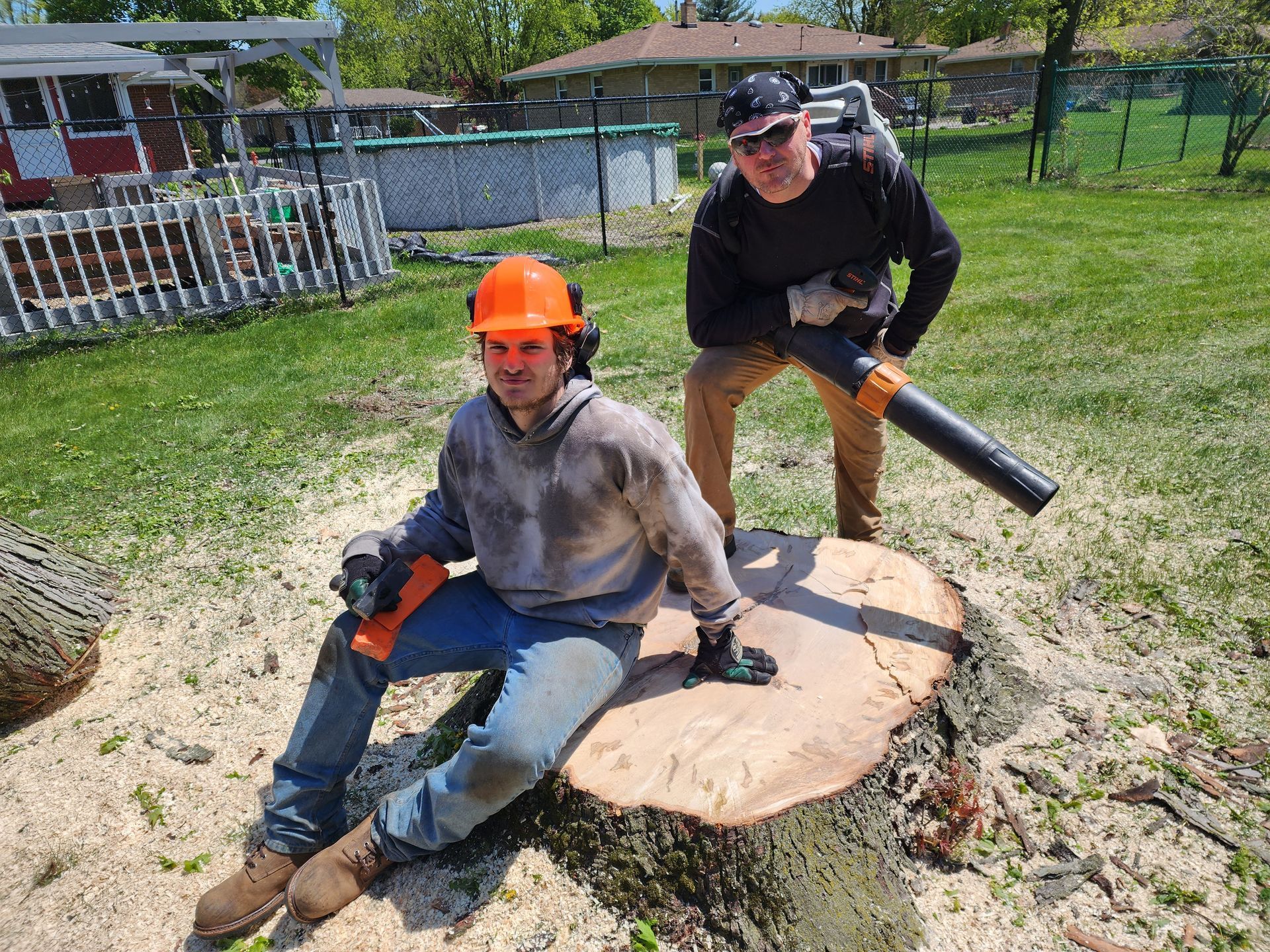 Two men are standing next to each other on a tree stump.