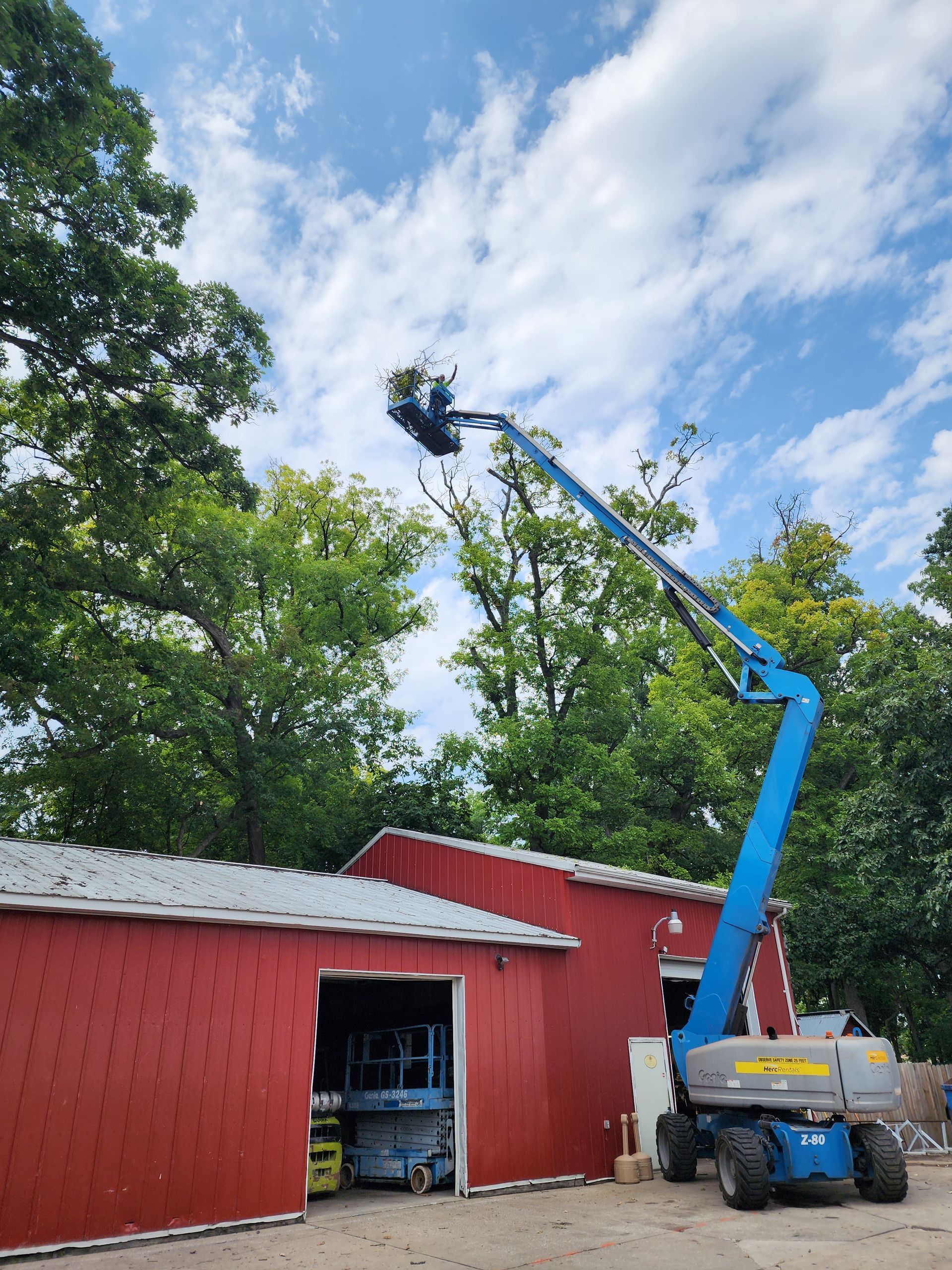 A blue crane is sitting in front of a red barn.