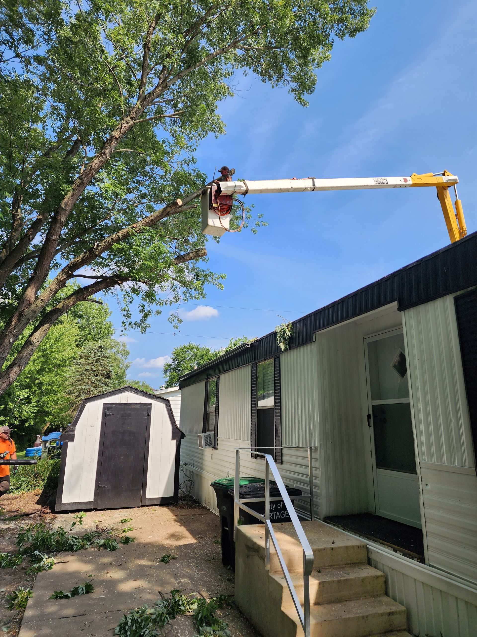 A man is cutting a tree in front of a mobile home.