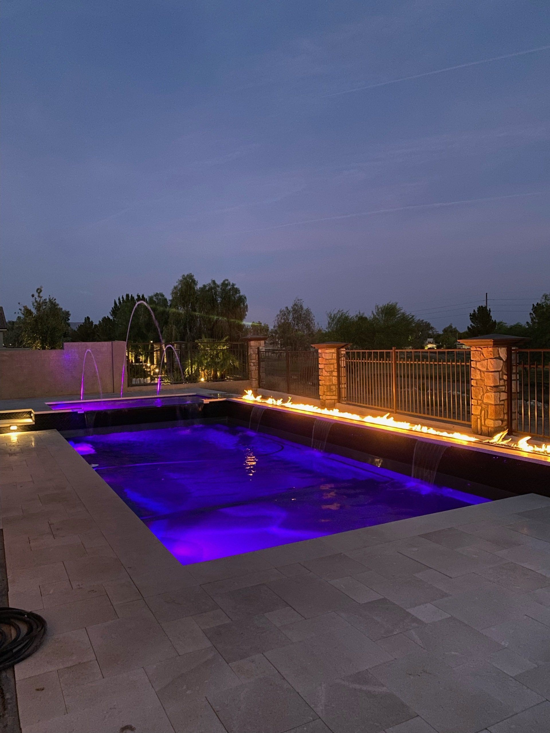 A large swimming pool is lit up with purple lights at night.
