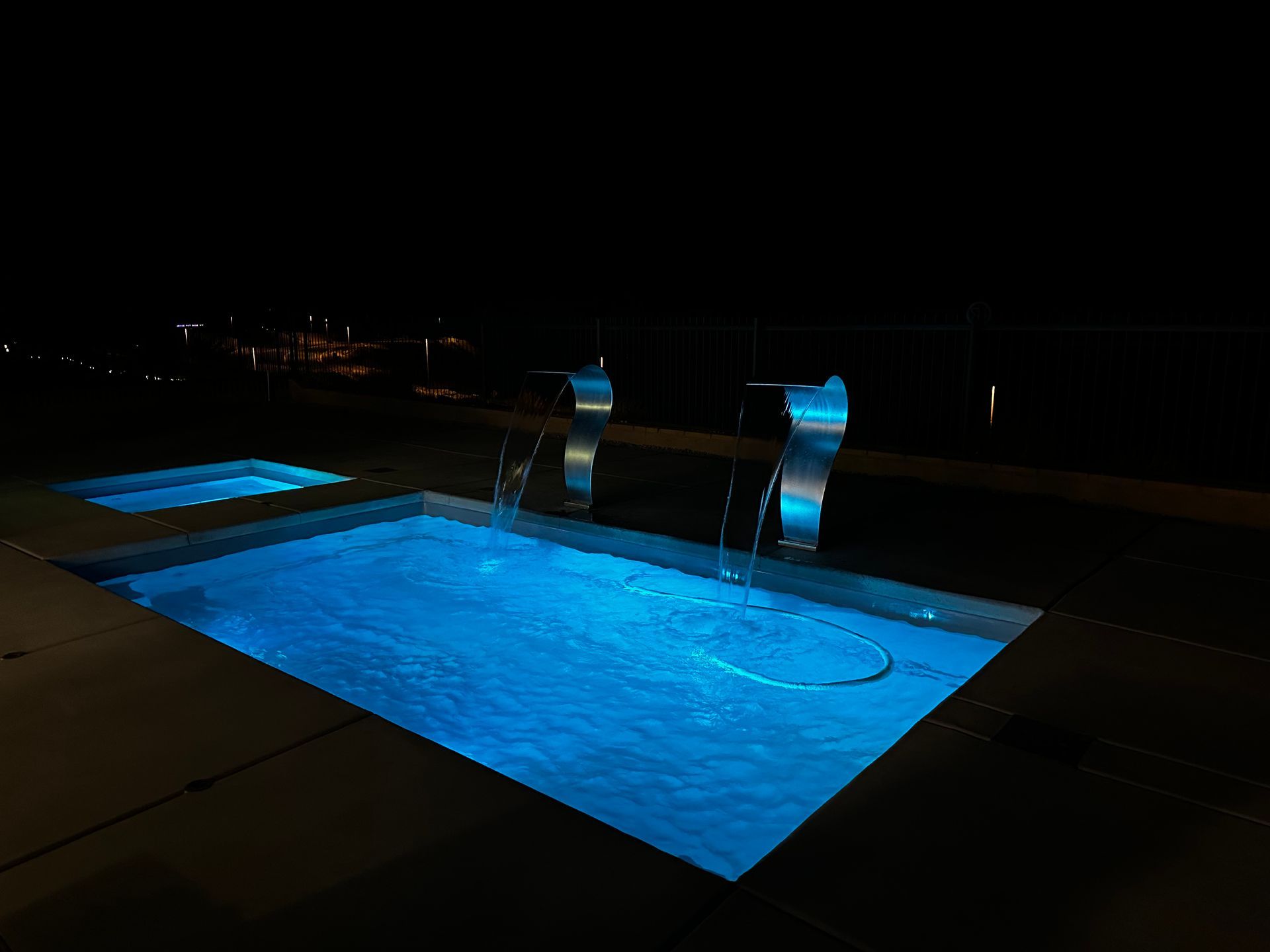 A swimming pool is lit up at night with blue lights.