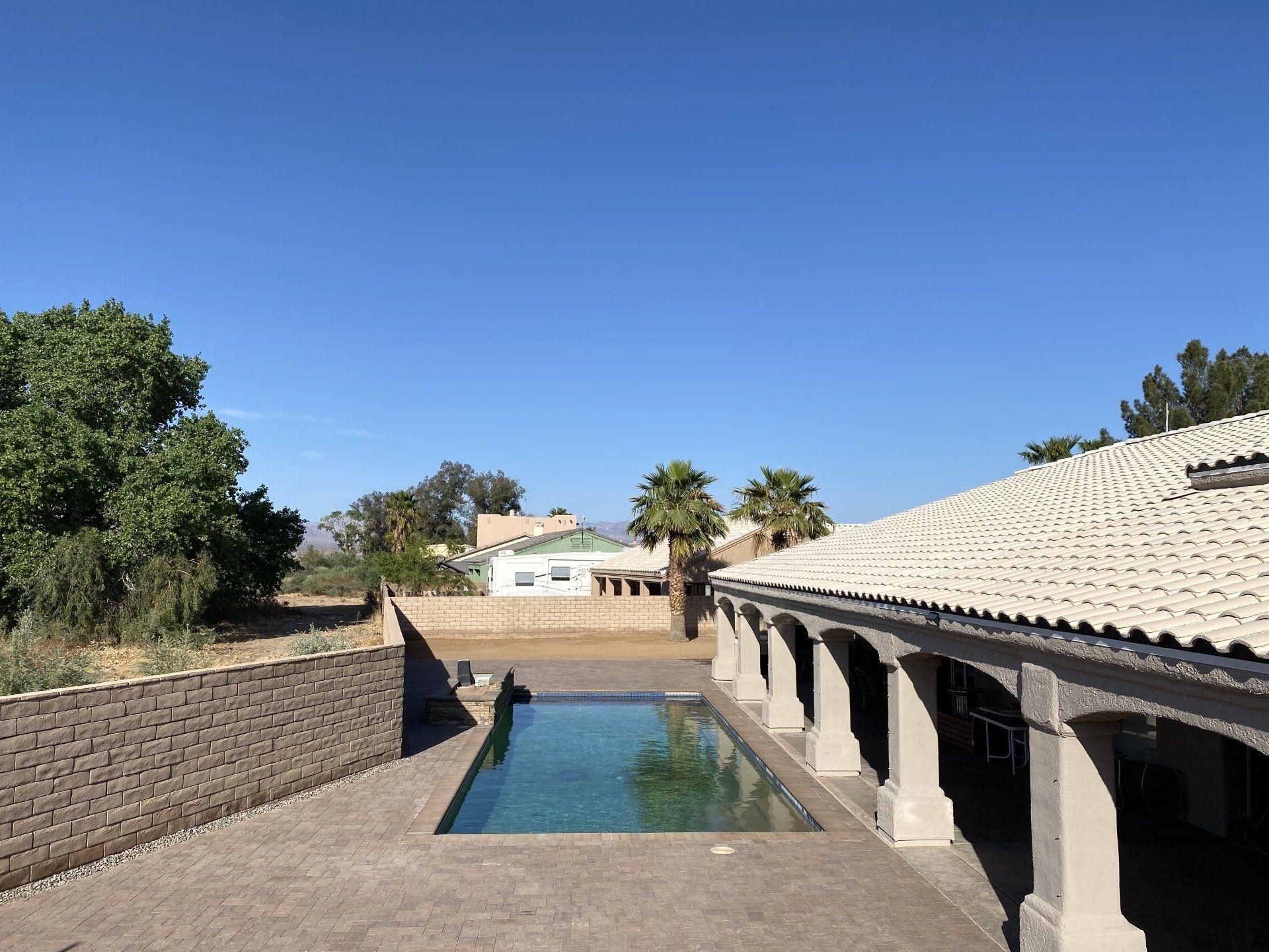 A large swimming pool is surrounded by a brick wall and a roof.
