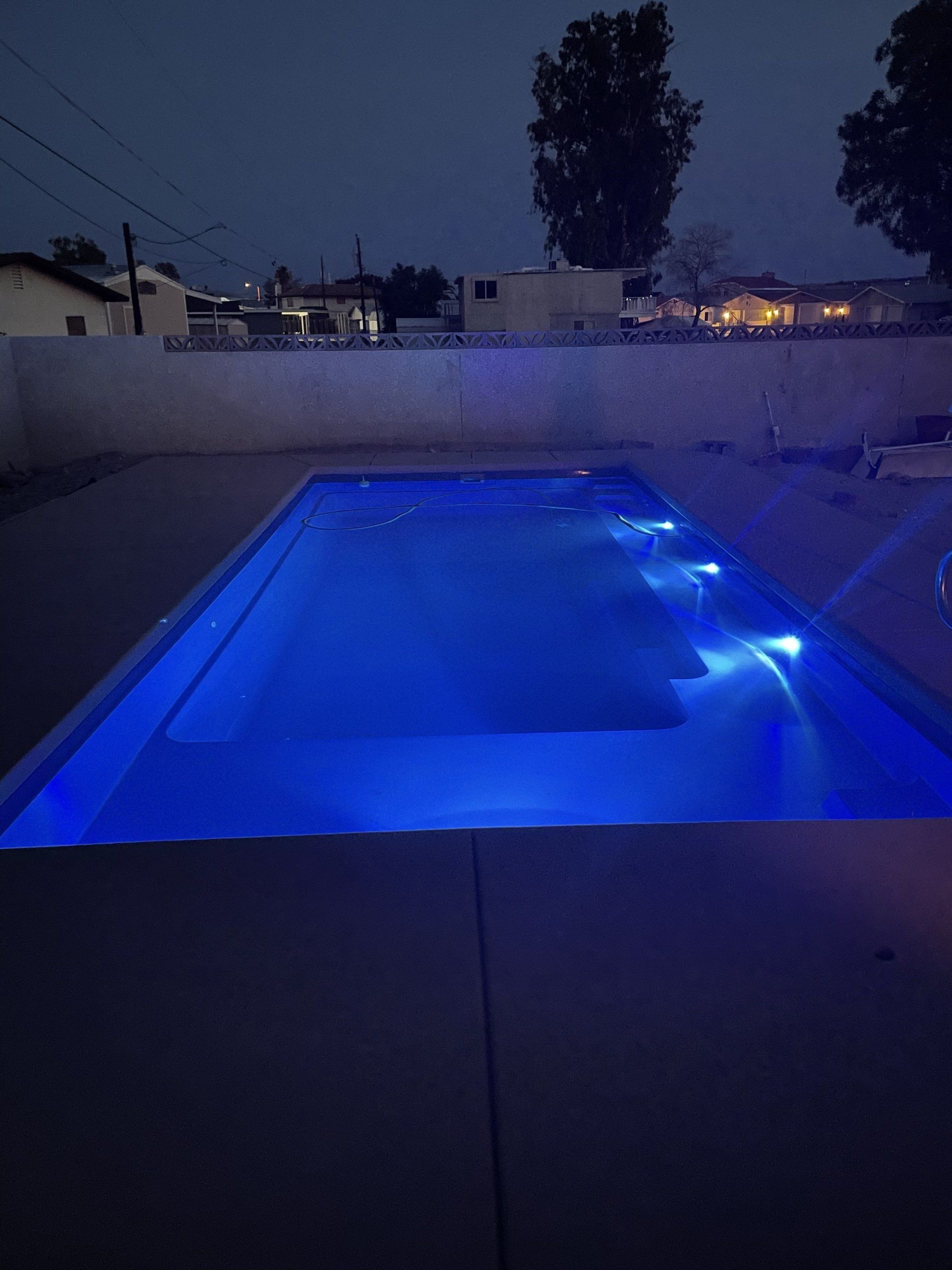 A large swimming pool is lit up with blue lights at night