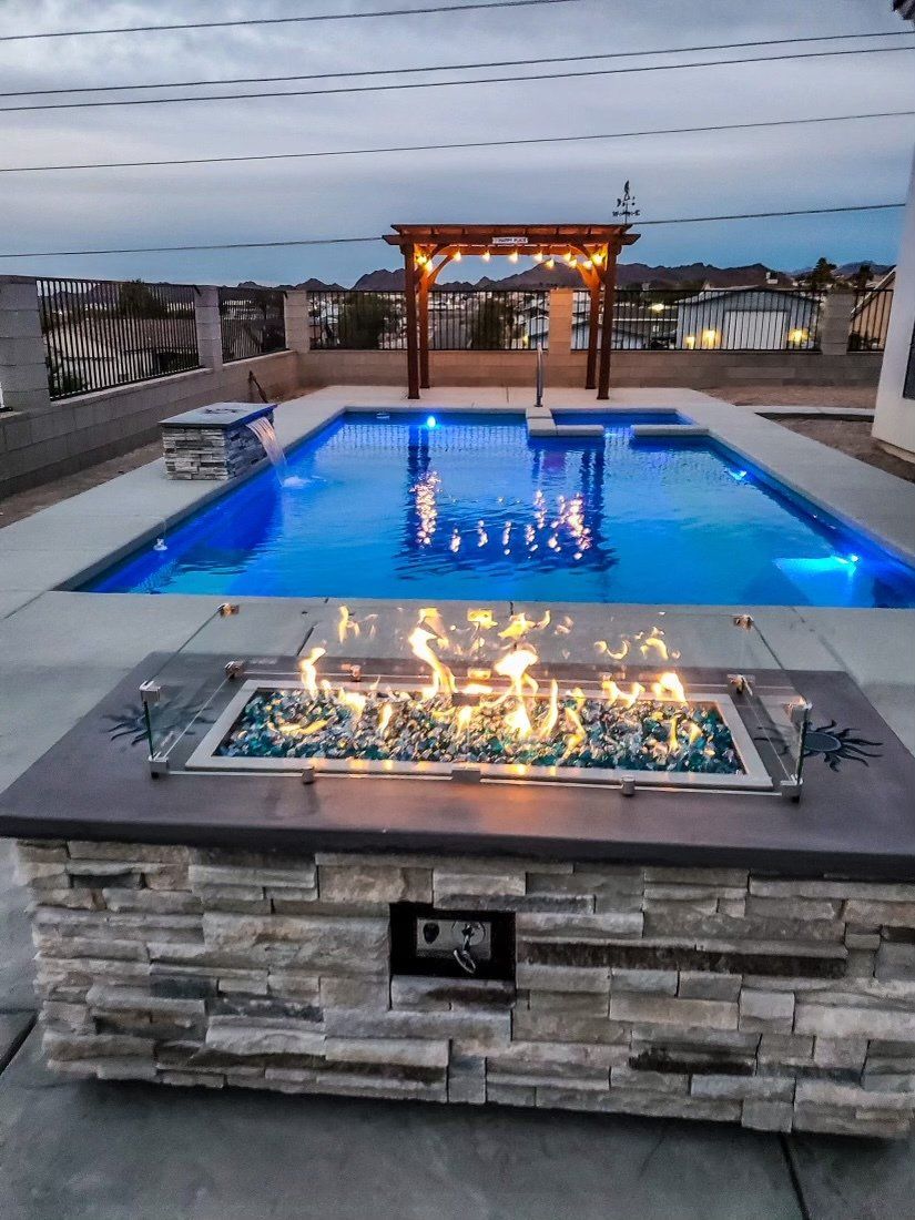 A fire pit in front of a large swimming pool