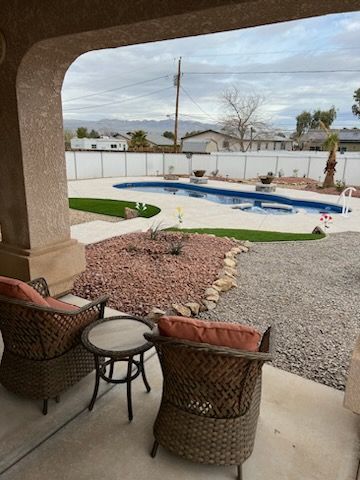 A patio with chairs and a table with a pool in the background.