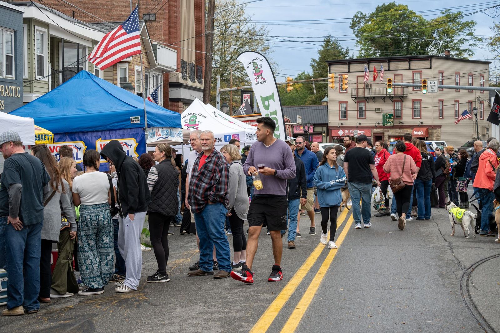 Crowded outdoor street market with tents, flags, and people lining both sides of the road