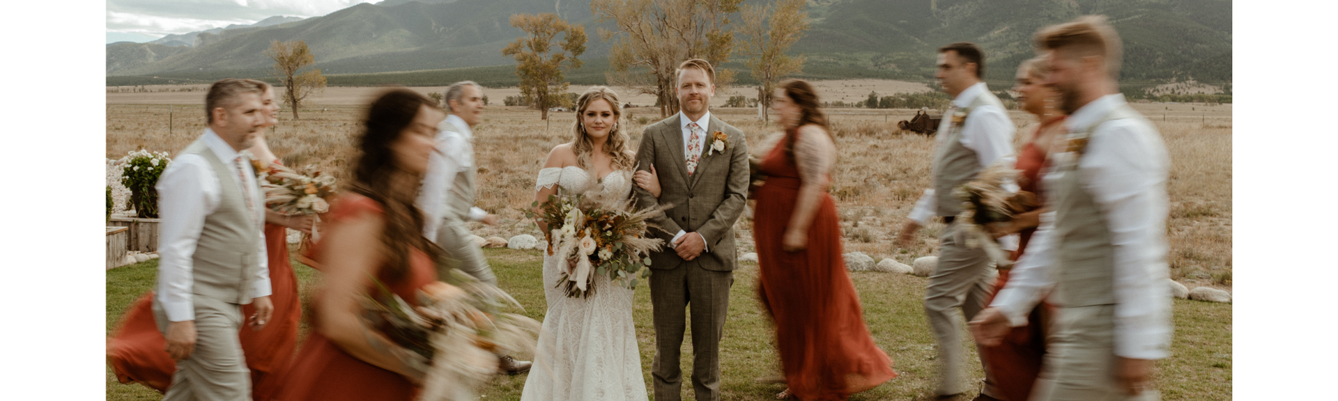 People in formal attire dancing outdoors near a lake and trees at a wedding celebration