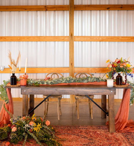 Rustic wooden table with autumn floral arrangements and decorations in a barn-like indoor setting