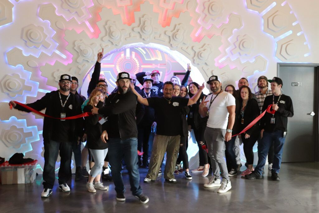 Group cuts red ribbon at an event, celebrating an opening in front of an art installation with lights.