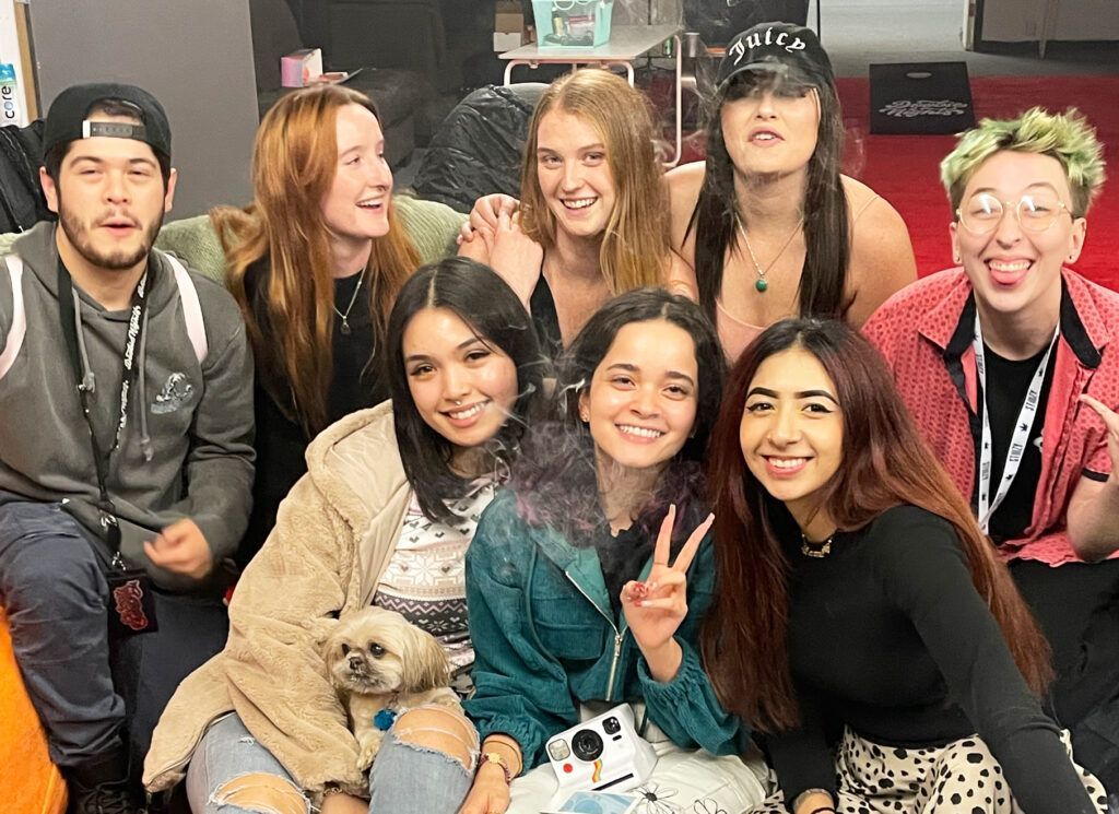 Group of nine young people smiling at the camera; a small dog sits in the foreground. They appear to be at an event.