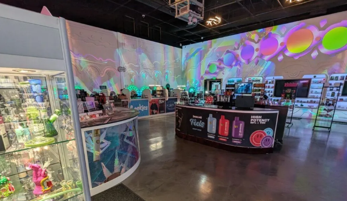 Interior of a brightly lit vape shop with colorful projections on the wall. 