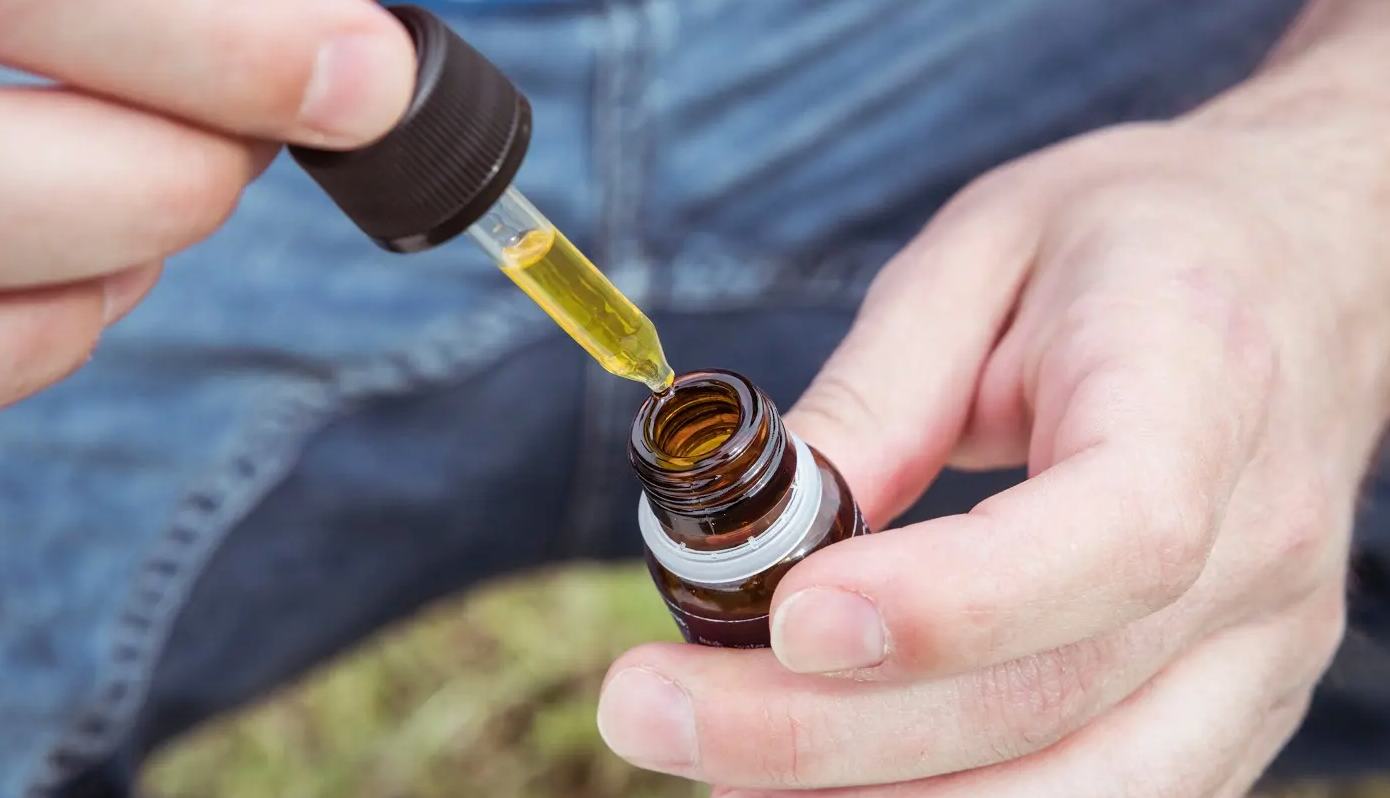 Close up of someone holding and opening a tincture bottle and pulling the dropper full of golden liquid out.