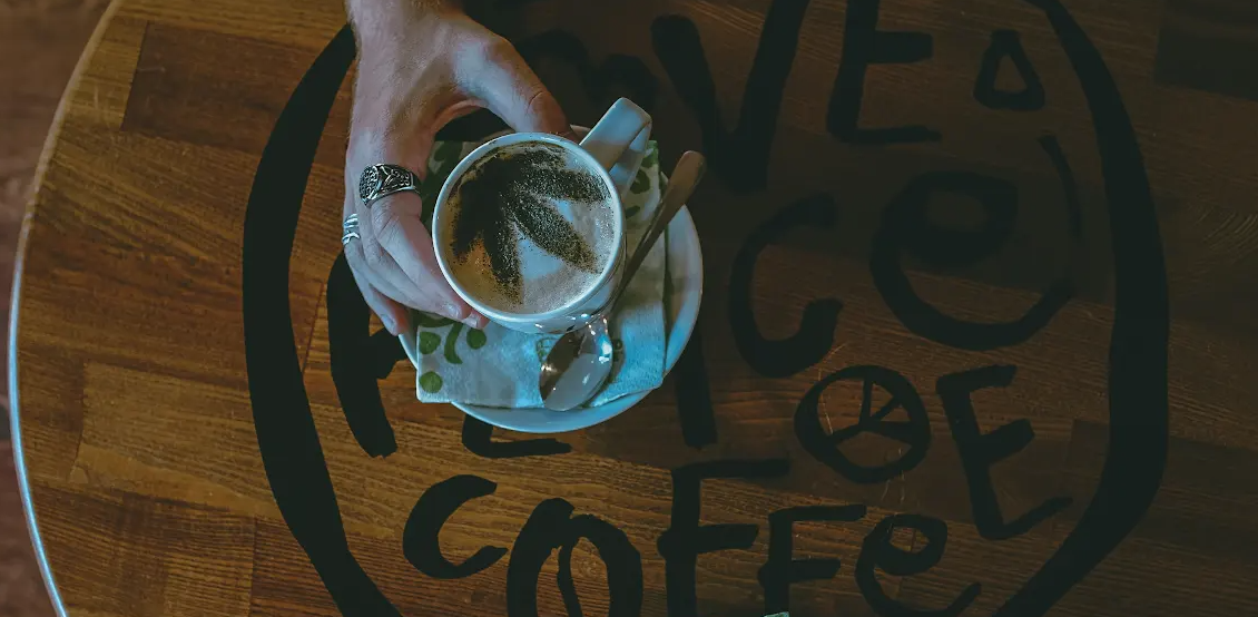 A cup of tea on a saucer, held by a hand, shown from above against a dark table.