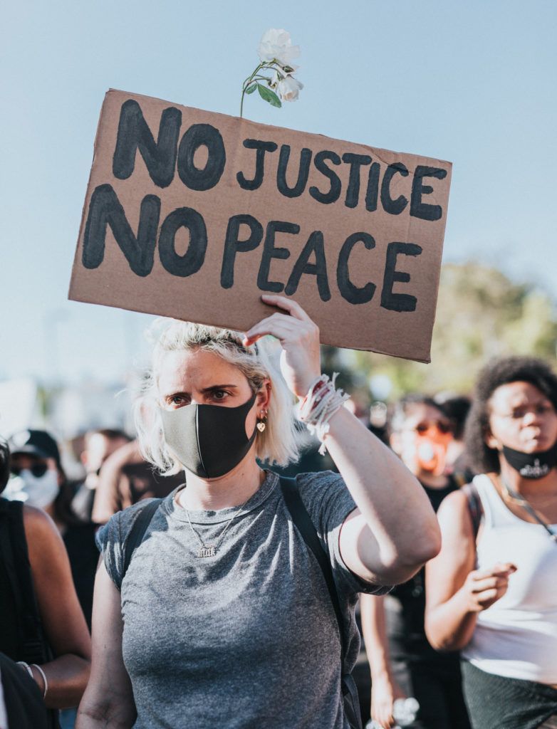 Protester in gray shirt and black mask holds a sign reading 