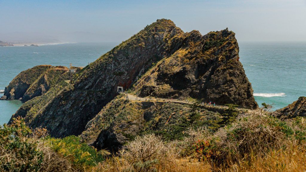 Rocky coastal outcrop with a tunnel, path, and ocean views under a sunny sky.