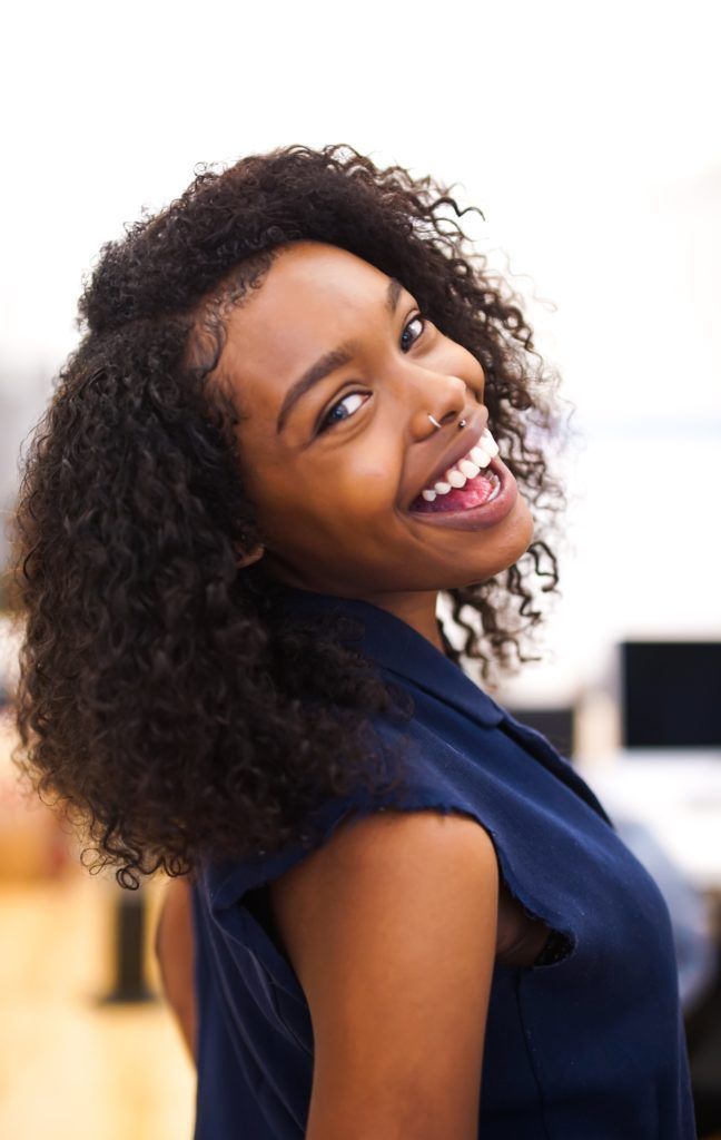 Smiling Black woman with dark curly hair, wearing a navy top, looking over her shoulder.