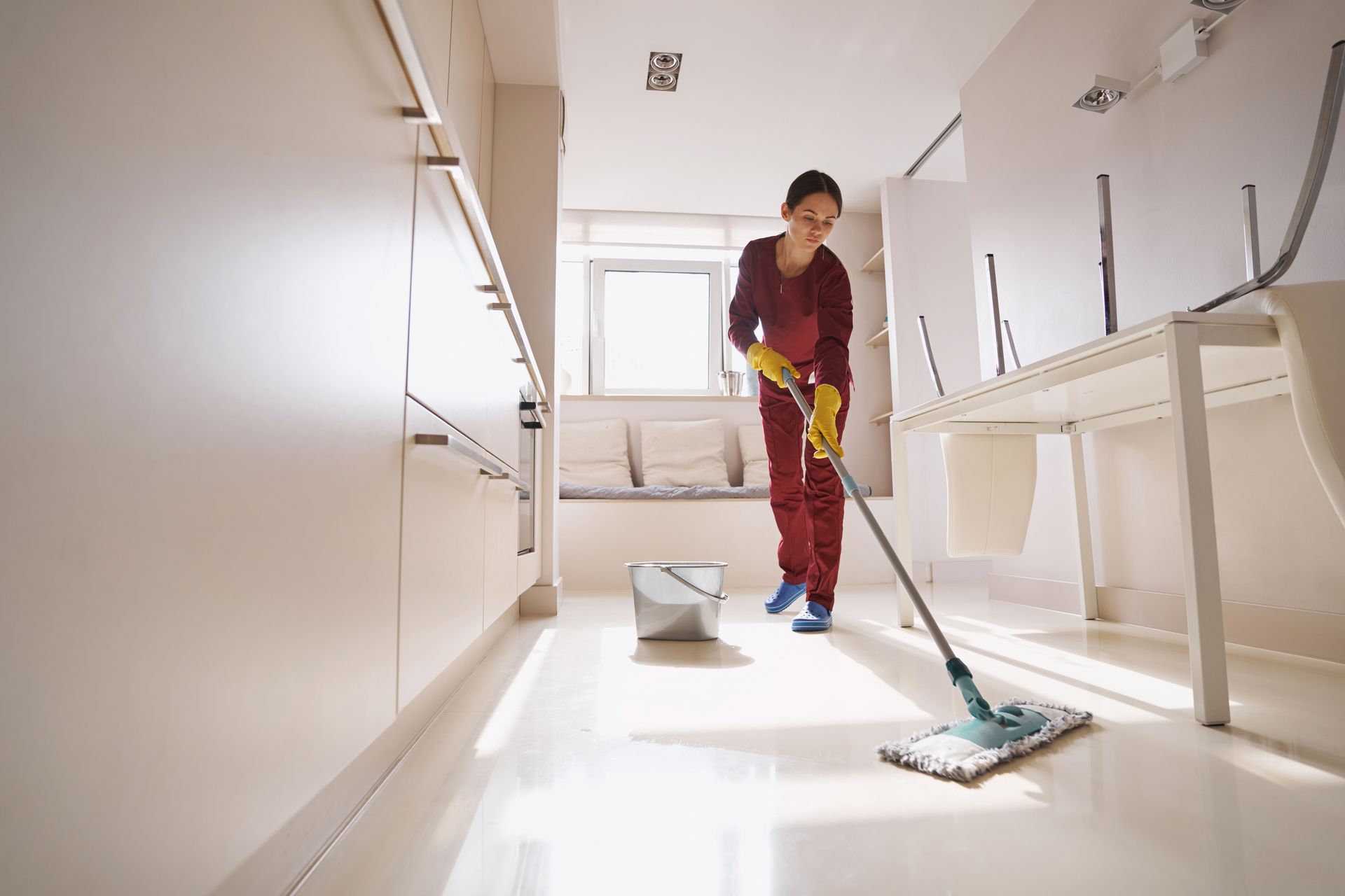 A concentrated, uniformed janitor is mopping the floor, performing janitorial cleaning services.