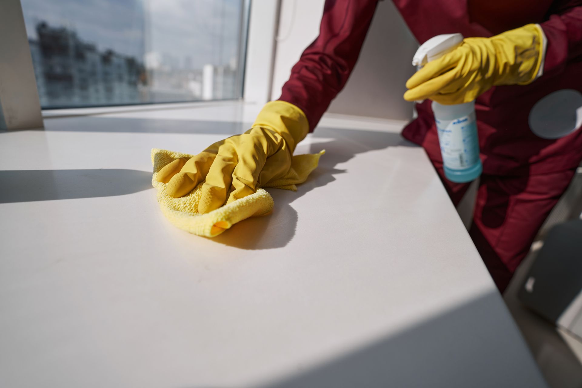 Cleaner in yellow gloves wiping a window sill
